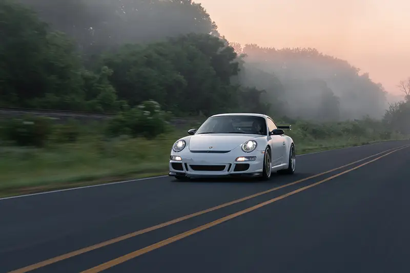 Photographie de Greg Banek d'une Porsche roulant sur une route entouré d'une forêt via Unsplash.