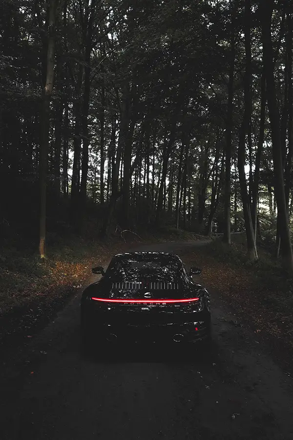 Photographie de Louis Meeckers d'une Porsche roulant sur un chemin forestier via Unsplash.