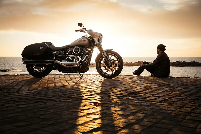 Un homme regarde un coucher de soleil à côté de sa Harley-Davidson